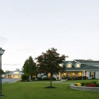 A picturesque landscape with a house, well-maintained lawn, and trees under a clear sky.