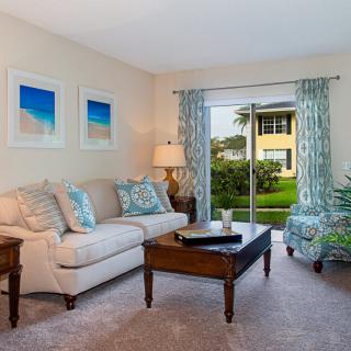 A cozy living room with a sofa, coffee table, and artwork, featuring a view of the outdoors through a sliding glass door.