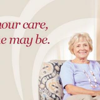 An elderly woman smiles comfortably while sitting in her living room.