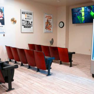 An empty waiting area with theater-style seating and a television on the wall, decorated with movie posters.