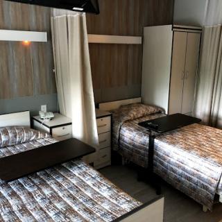 A shared hospital room featuring two beds, a wardrobe, and a television.