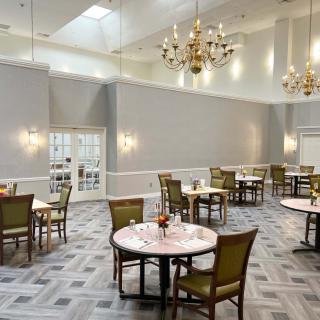 An elegant dining room with chandeliers, neatly arranged tables, and chairs on a patterned carpeted floor.