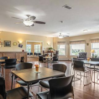 A spacious dining area with tables and chairs, illuminated by ceiling fans and natural light from large windows.