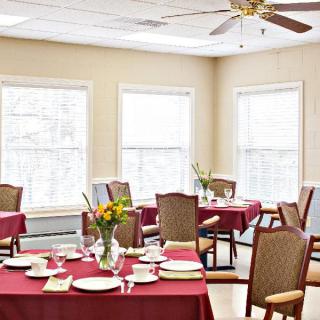 A brightly lit dining room with tables set for a meal, featuring red tablecloths and floral centerpieces.