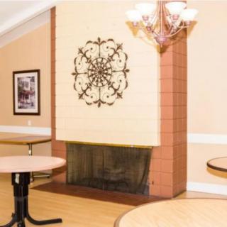 A cozy indoor space featuring a fireplace adorned with decorative artwork, round tables, and a chandelier.