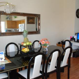 A well-decorated dining room with a dark table, surrounded by chairs and adorned with a fruit basket and flowers.
