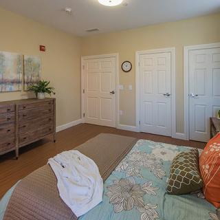 A cozy bedroom interior featuring a bed with colorful pillows, a wooden dresser, and wall art.