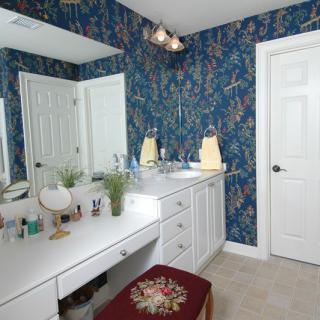 A bathroom with a floral-patterned wallpaper, a white vanity with a mirror, and various toiletries on the counter.