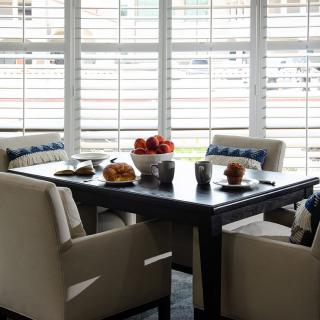 A cozy dining area with a table set for breakfast, featuring comfortable chairs and ample natural light from nearby windows.