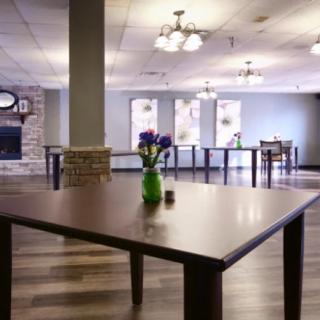An empty dining area with wooden tables and a vase of flowers in a bright, spacious room.