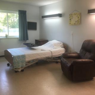 A well-lit hospital room featuring a patient bed, an armchair, and a window.