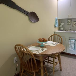 A cozy dining area with a wooden table and chairs set for two, featuring a large spoon decoration on the wall.