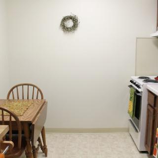 A cozy kitchen featuring a dining area with a wooden table and chairs, along with a stove and decorative wreath on the wall.