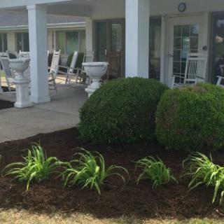 A beautifully landscaped garden with neatly arranged bushes and fresh mulch, adjacent to a patio with outdoor seating.