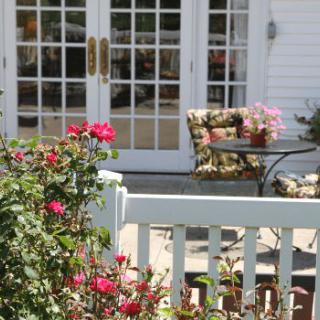 A cozy patio area with a table and chairs, surrounded by blooming roses and flowers, next to glass doors.