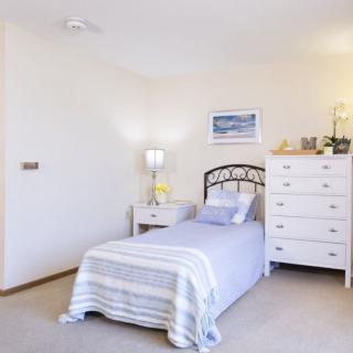 A cozy bedroom with a single bed, white furniture, and minimalist decor.