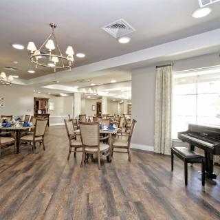 A well-lit dining area with elegant tables and chairs, featuring a piano and a chandelier.