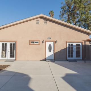 A one-story house with a paved driveway and multiple windows under bright daylight.