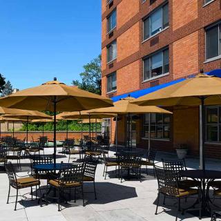 Outdoor patio area with tables and umbrellas at a building on a sunny day.
