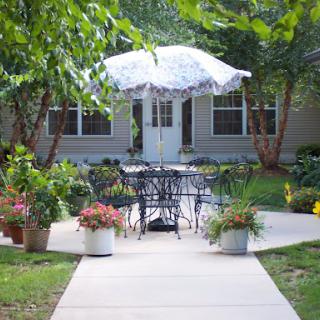 A serene outdoor patio area furnished with a table and chairs, surrounded by lush greenery and blooming flowers.