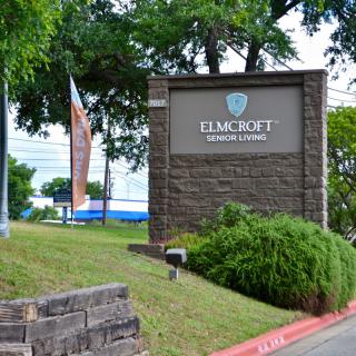 A stone sign with landscaping and trees in the background.