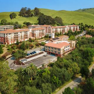 Aerial view of a large building complex surrounded by lush greenery and hills.