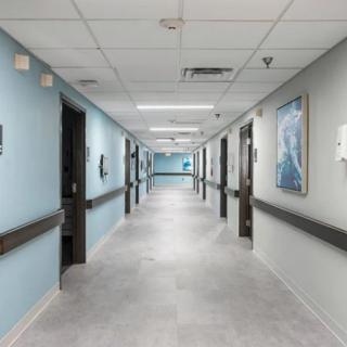 A clean and empty hospital corridor with blue walls and multiple doors.