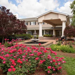 A beautiful garden with vibrant flowers and a fountain in front of a large building.