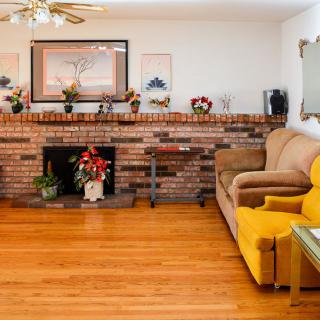 A cozy living room featuring a brick fireplace, yellow chair, and hardwood floors.
