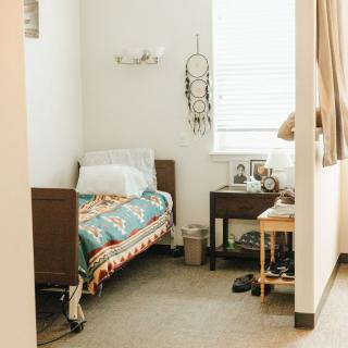 A cozy bedroom featuring a single bed with a colorful blanket, a dreamcatcher on the wall, and a nearby nightstand with a lamp.