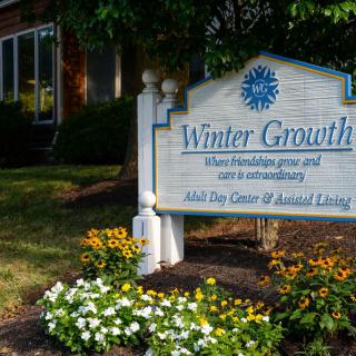 Sign outside a building surrounded by flowers and greenery.