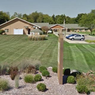 A suburban residential area with neatly mowed lawns, a driveway, and parked cars.