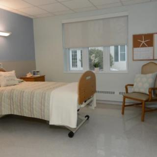 A clean and minimalist hospital room with a single bed and a chair.