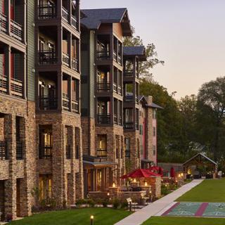 A scenic view of an apartment building with balconies, surrounded by greenery and outdoor seating areas in the evening light.