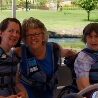 A group of three people wearing life jackets, sitting outdoors and smiling.