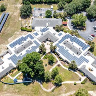 Aerial view of a building complex with solar panels on the rooftops, surrounded by greenery.