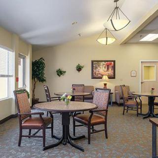 A well-lit room with tables and chairs arranged for dining or meetings, featuring soft lighting and decorative wall elements.