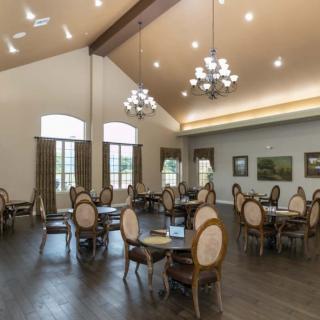 A spacious dining area with elegant tables and chairs, illuminated by chandeliers and natural light from large windows.