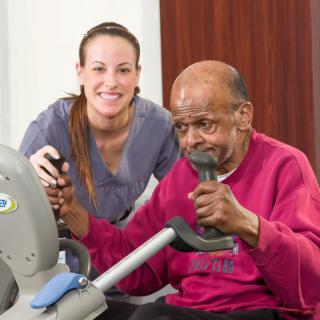 An elderly man exercising with the assistance of a healthcare worker.
