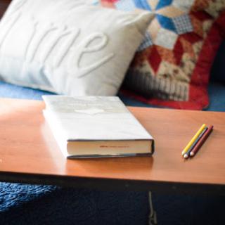 A cozy reading spot featuring a book, a decorative pillow, and a yellow pencil on a wooden table.