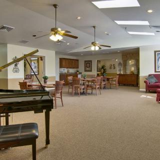 A spacious room featuring a grand piano, ceiling fans, and a seating area with tables and chairs.
