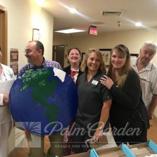 A cheerful group of staff members at Palm Garden, gathered around a globe to celebrate unity and care.