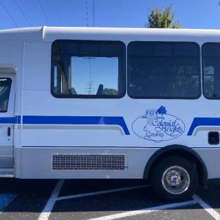 A white bus with a blue stripe parked in a parking lot, featuring a logo on its side.