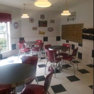 A retro-style diner with red chairs, round tables, and a checkerboard floor.