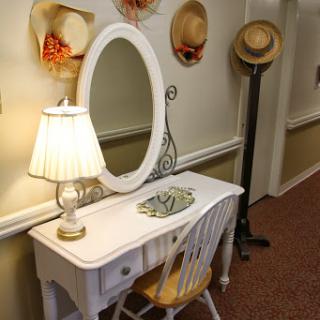 A charming vanity table with a mirror, lamp, and decorative hats adorning the wall.
