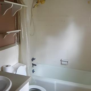 A bathroom with a bathtub, sink, toilet, shelves, and a mirror.