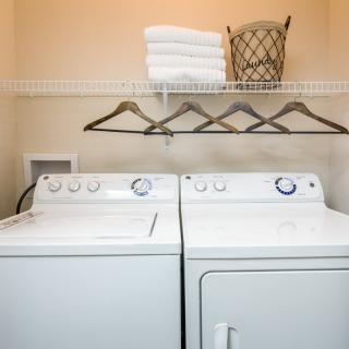 A laundry room featuring a washing machine and dryer underneath a shelf with neatly folded towels, hangers, and a wicker basket.
