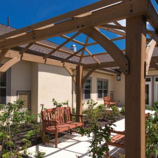 A sunny patio with a wooden pergola and comfortable seating surrounded by greenery.