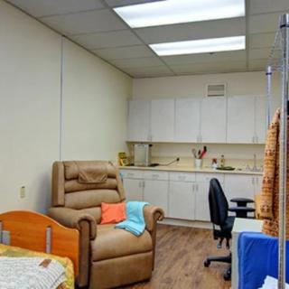 A clinic treatment room with a recliner chair, desk, and cabinets.