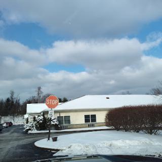 A serene winter scene featuring a snow-covered building and a stop sign under a cloudy sky.
